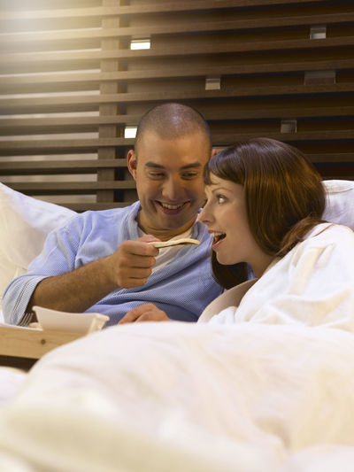 Smiling mid adult couple having food on bed at home