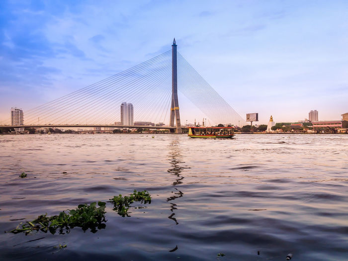 Suspension bridge over river in city against sky