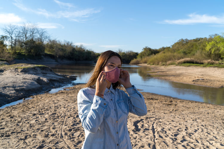 Portrait of young woman holding her protective mask on the beach