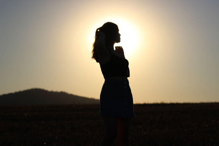 Woman standing on field against clear sky during sunset