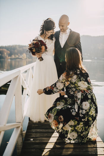 Bridesmaid helping wedding couple on jetty over lake