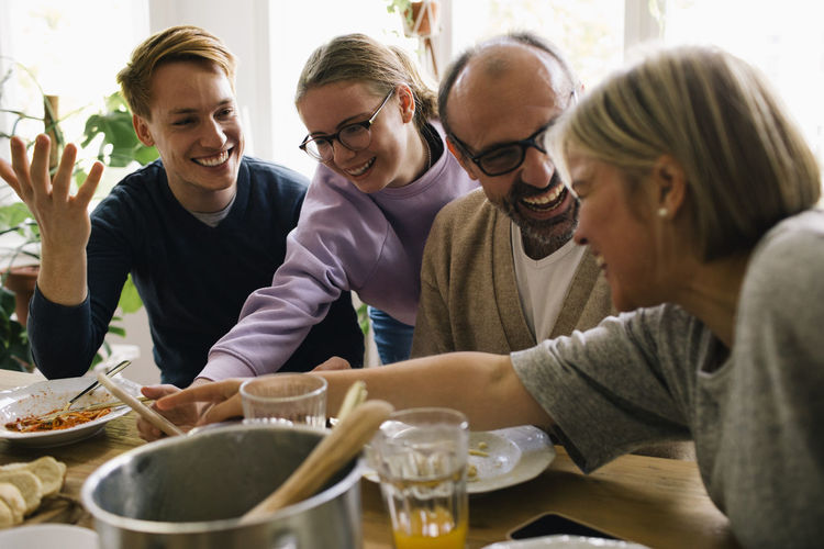 Happy family enjoying meal together while sharing smart phone at home