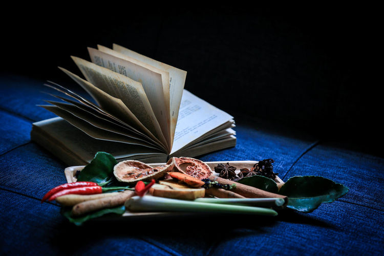 Close-up of dried ingredients by book on table against black background