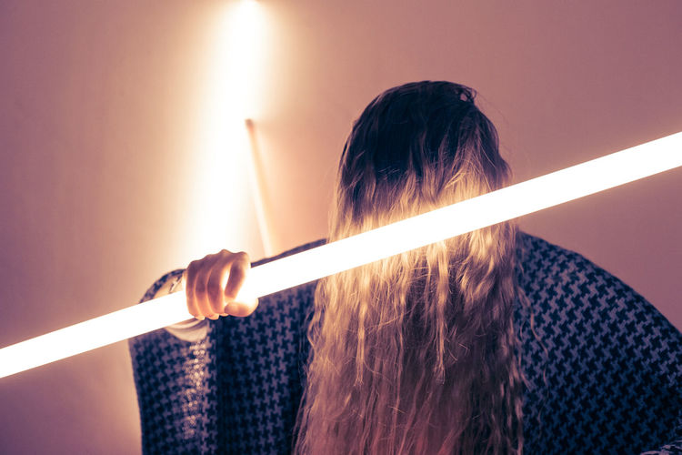Woman holding illuminated fluorescent light against wall