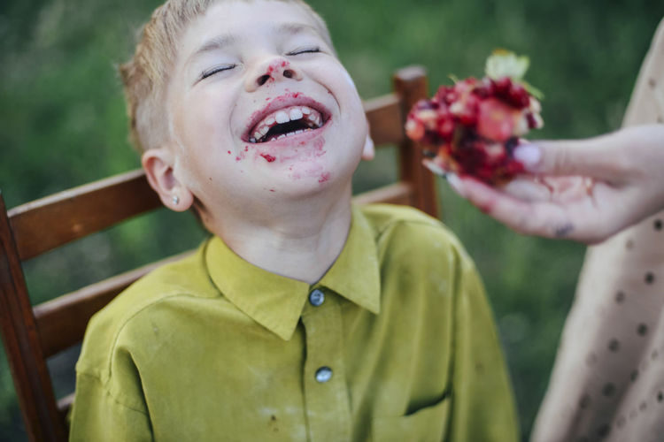 Cropped hand of mother feeding sweet pie to happy son sitting on chair at yard