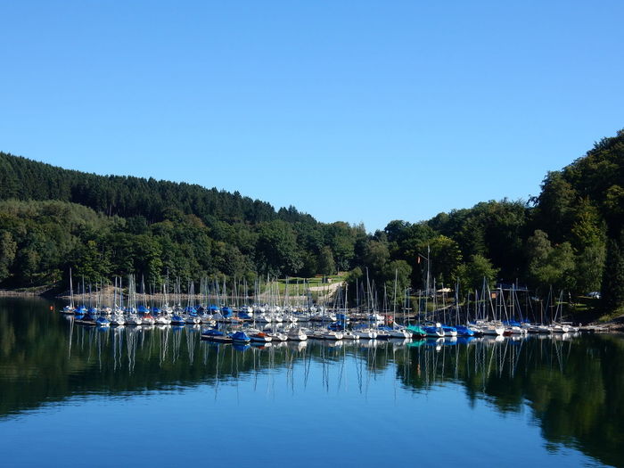 Boats moored in lake against clear blue sky