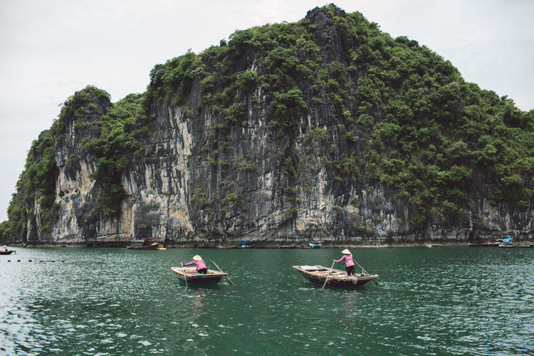 People rowing boat on halong bay by mountains