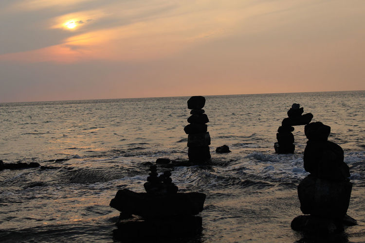 Silhouette stack rocks at beach against sky during sunset