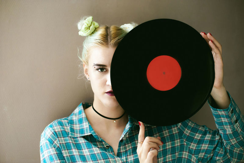 Portrait of young woman holding record against beige background