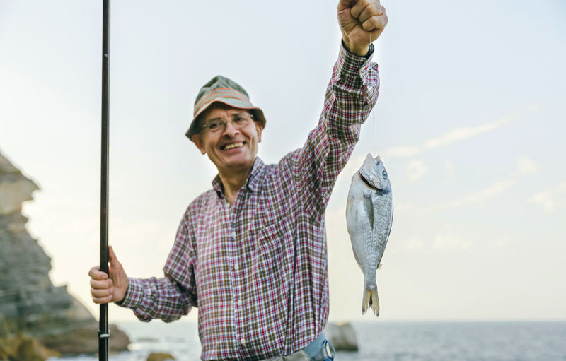 Happy senior man holding fish on fishing line