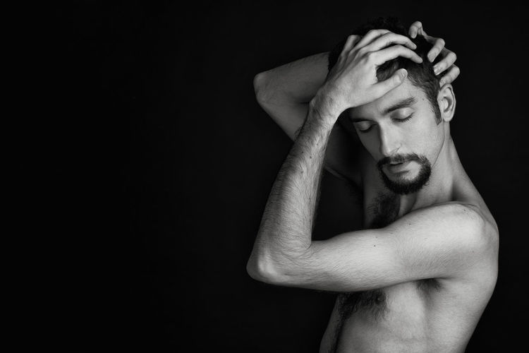 Portrait of shirtless young man against black background