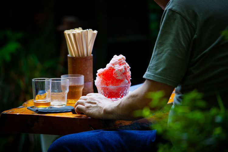 Midsection of man eating kakigoori sitting on table