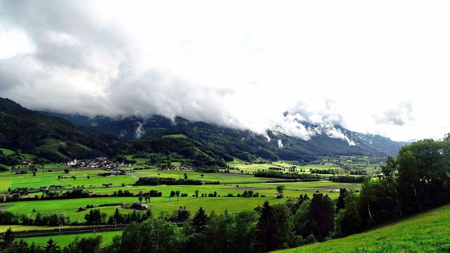 Scenic view of green landscape and mountains against cloudy sky
