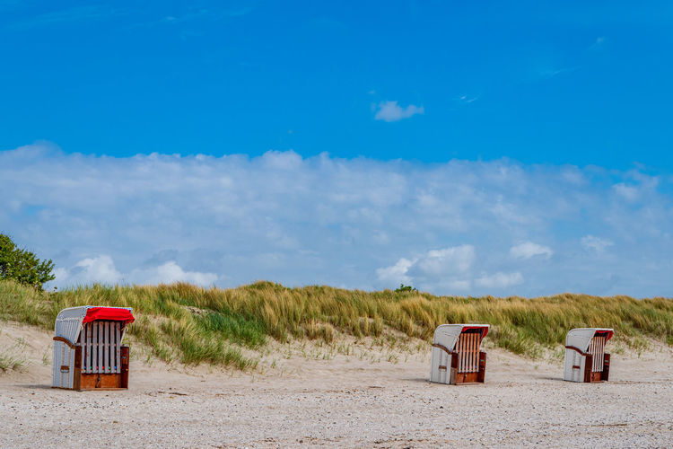 Hooded chairs on beach against blue sky