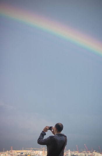 Rear view of man photographing rainbow