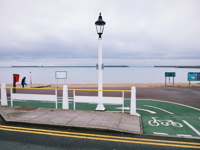 Street light by bicycle lane at beach against cloudy sky