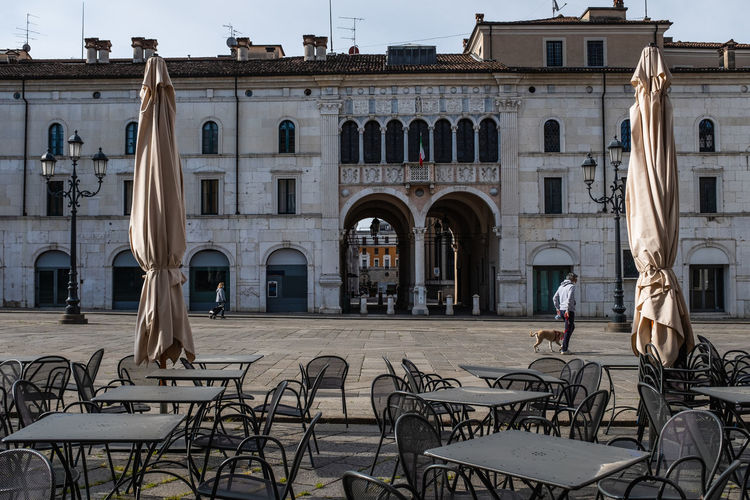 Empty tables and chairs outside a restaurant. two people walking in the main town square in brescia. 