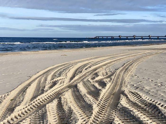 Tire tracks on beach against sky