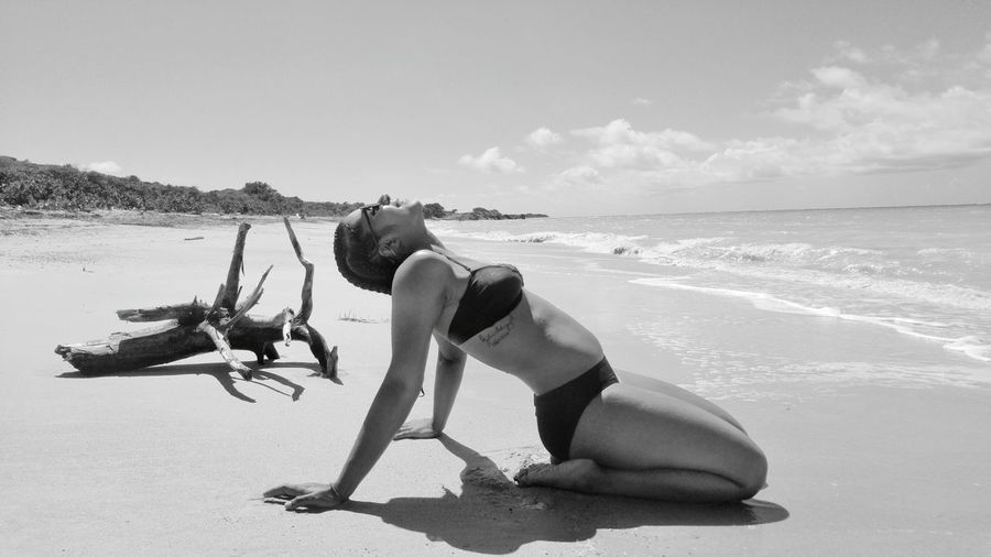 Woman wearing bikini while kneeling on sand at beach