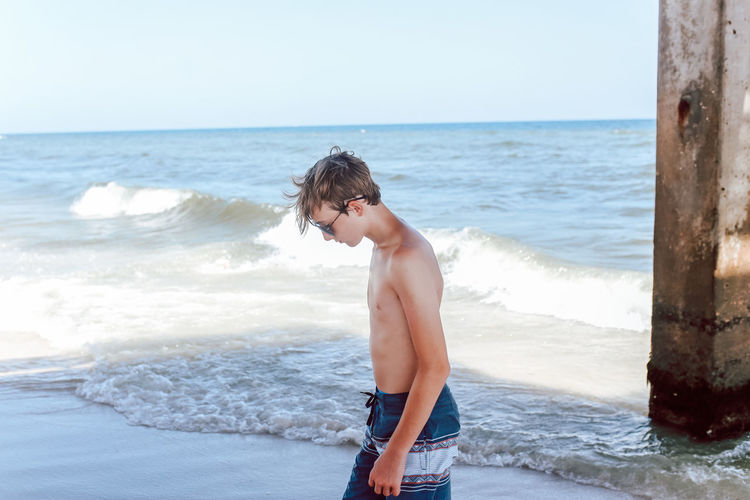 Full length of shirtless boy standing at beach against sky