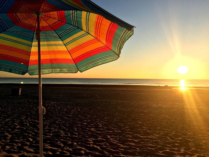 Colorful parasol at sandy beach against clear sky during sunset