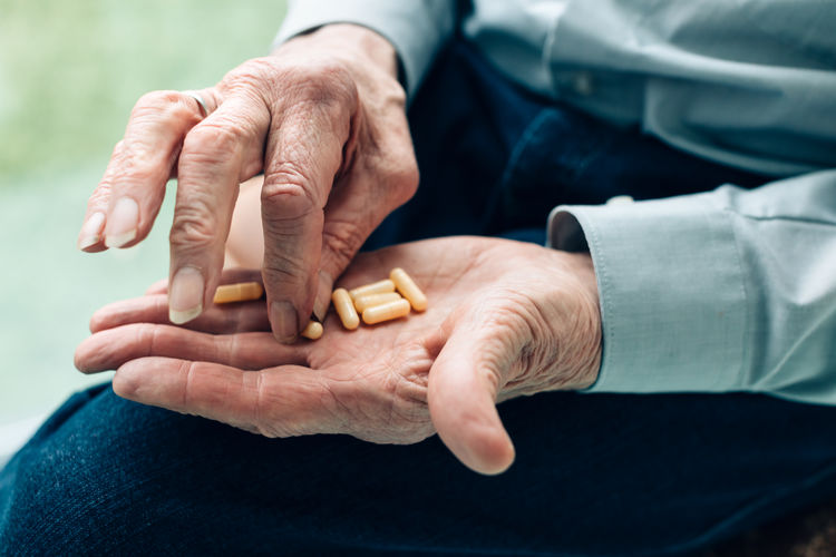 Senior man holding drug pills for medication - focus on hands