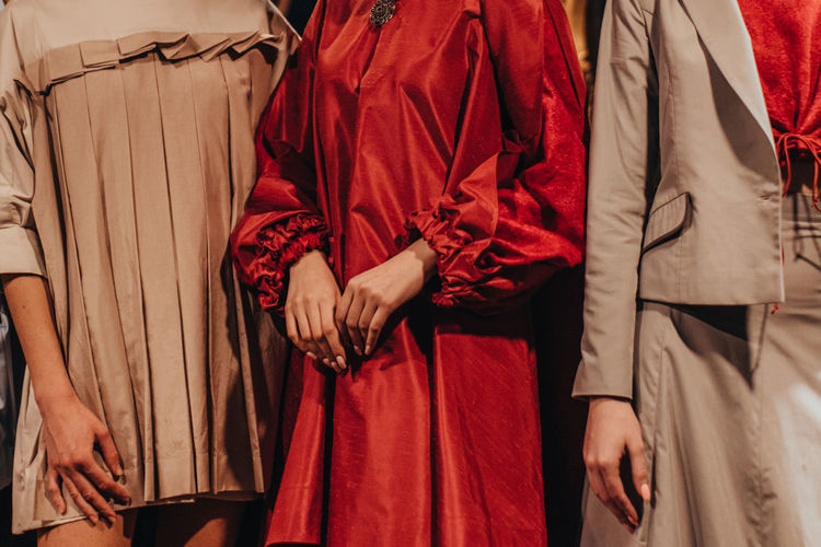Three female fashion figures in red and beige casual stylish outfits, pants, sweaters on backstage 