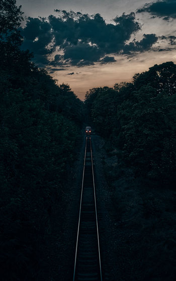 Train on railroad track amidst trees against sky during sunset