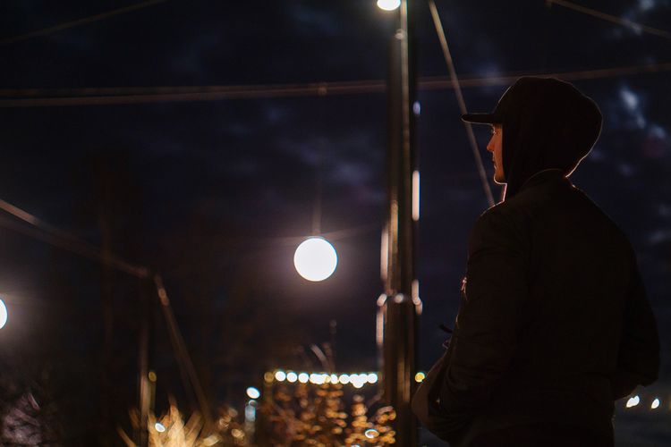 Rear view of man standing by illuminated lights at night