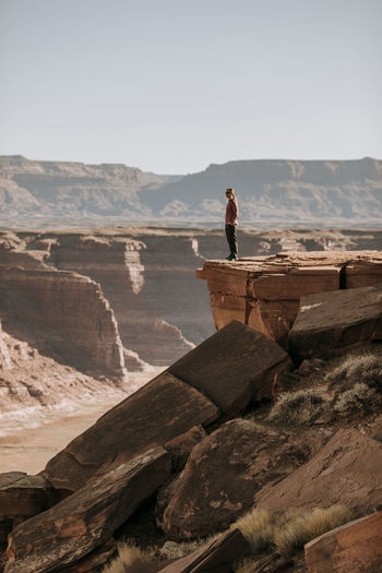 Woman stand on edge of high cliff looking over desert, hite, utah