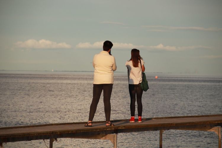 Rear view of friends standing on railing against sea