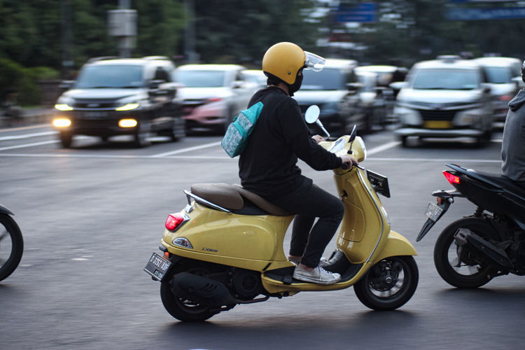 Rear view of man riding motor scooter on road