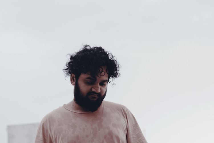 Thoughtful young bearded man standing against clear sky