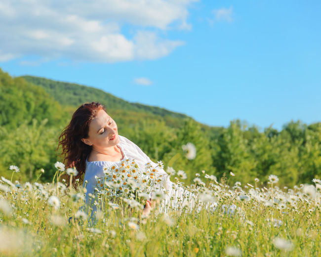 Portrait of young woman standing amidst flowering plants on field against sky