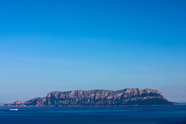 Scenic view of rock mountain by sea against clear blue sky