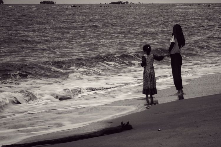 Rear view of teenage girl with sister standing at beach