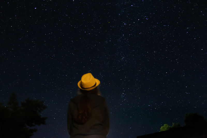 Back view of woman in yellow hat looking night sky with many stars. night sky silhouette of a woman