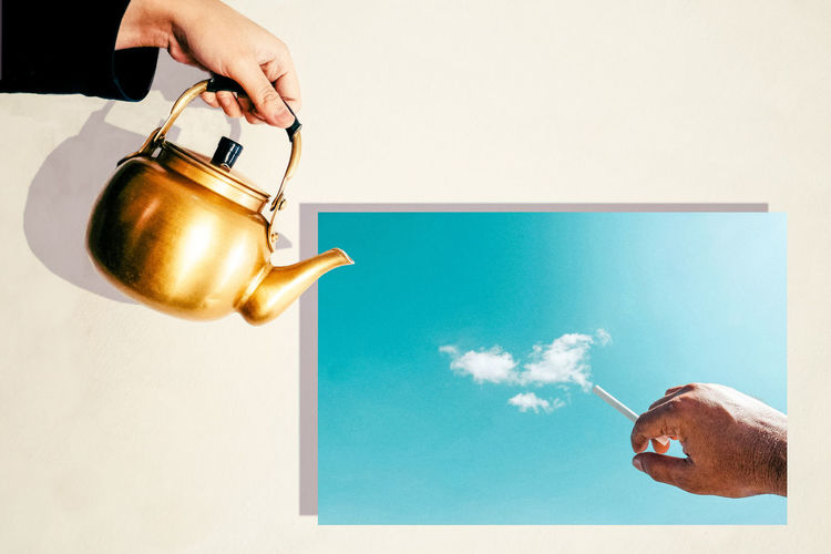 Optical illusion of hand holding tea kettle over photograph of man with cigarette emitting clouds