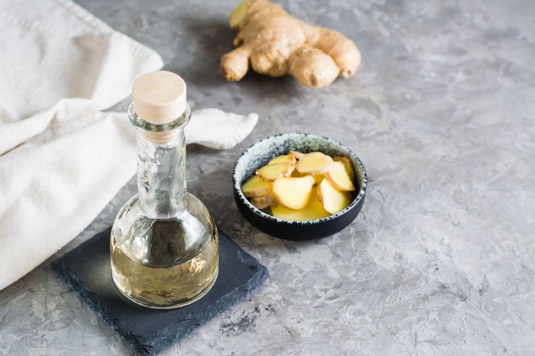 Bottle with natural ginger serum and chopped ginger in a bowl on the table. natural care cosmetics.