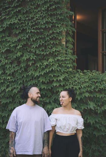 Woman sticking out tongue standing with boyfriend in front of green ivy plants