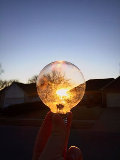 Optical illusion of hand holding bulb against sun during sunset