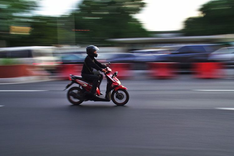 Full length of man riding motor scooter on street