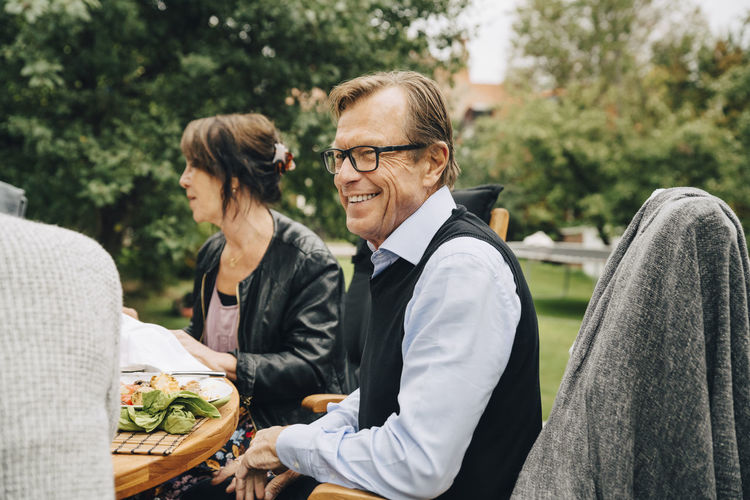 Smiling senior man sitting with friends at dining table in back yard