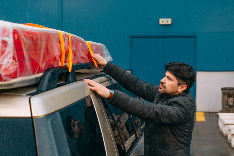 Man securing mattress on car top in a rainy evening