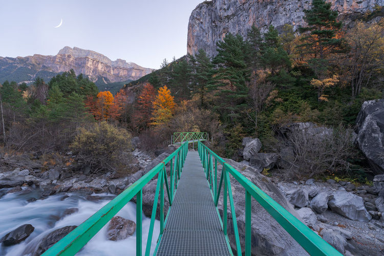 Narrow footbridge crossing fast mountain river in autumn evening sunset in ordesa y monte perdido national park in huesca, spain