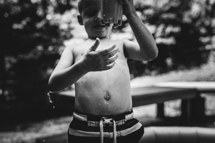 Midsection of shirtless boy holding tree