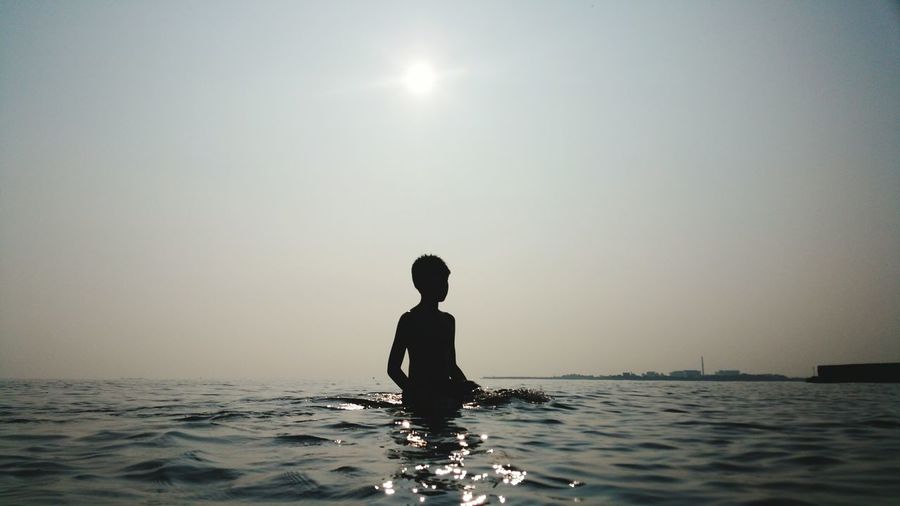 Silhouette boy standing in sea against clear sky