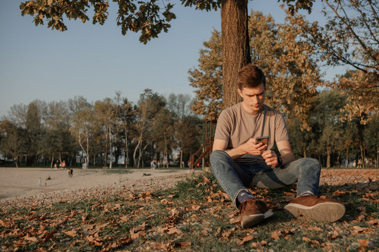Man sits on the stones beach and holds smartphone in the hands