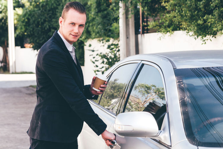 Portrait of businessman opening car door on road