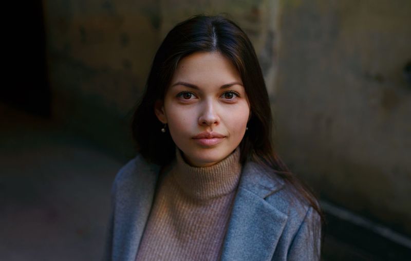 PORTRAIT OF BEAUTIFUL YOUNG WOMAN STANDING AGAINST BLURRED BACKGROUND